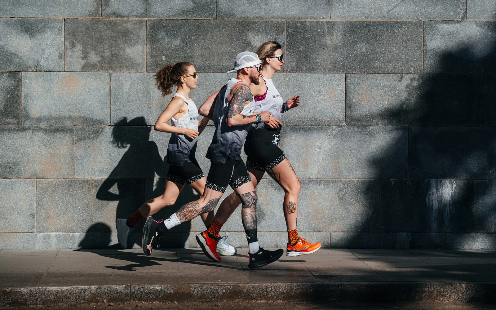 Трое бегунов в экипировке IN RUN WE TRUST бегут вдоль гранитной стены